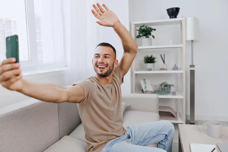 Happy man taking a selfie in a modern living room, showcasing self-expression and joy with a bright and stylish interior amidst a relaxed atmosphere.
