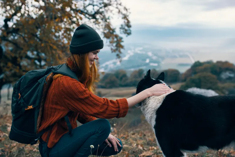 Женщина с рюкзаком на природе играет с собакой в горном пейзаже