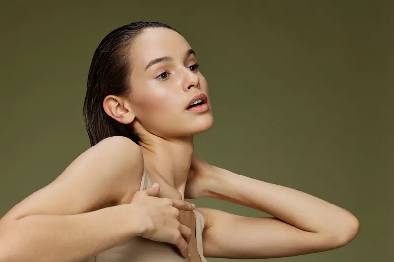 Elegant young model with wet hair posing gracefully against a soft green background, showcasing natural beauty and confidence in fashion forward attire