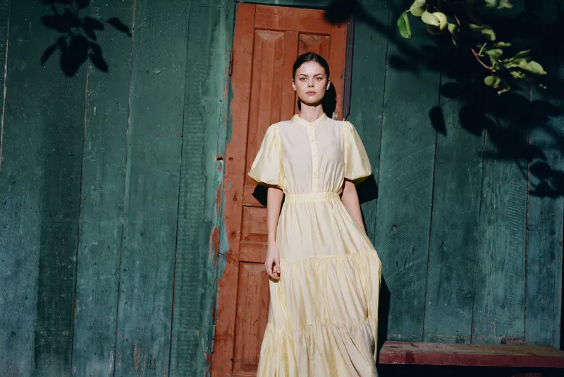 Woman standing in doorway in yellow dress rustic portrait fashion with sunlight inclusive