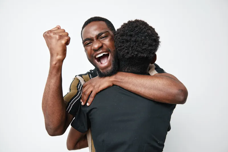 African American man with dark skin celebrating and hugging child with curly hair in studio. Joyful family moment with happiness and emotional connection on white background.
