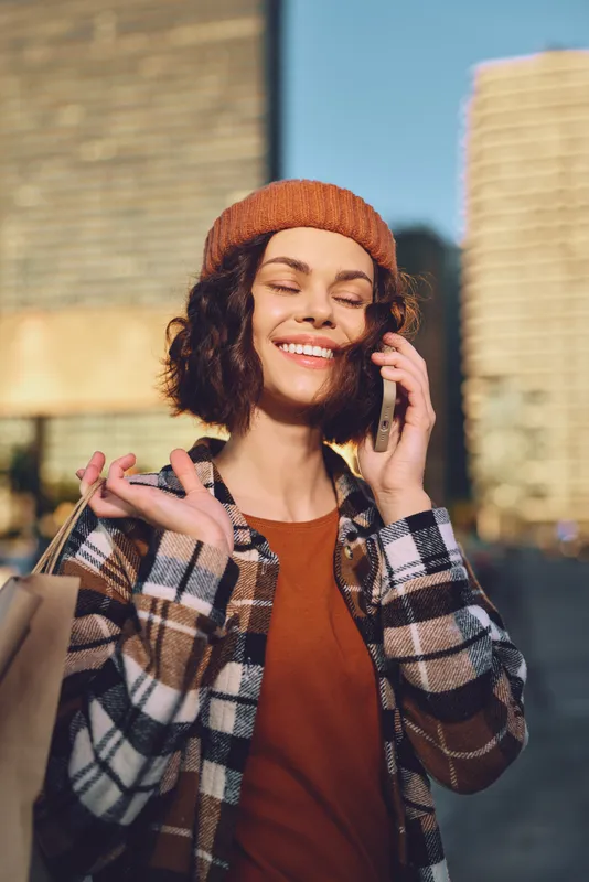 Woman smile on phone with shopping bags in urban portrait at golden hour sunlight, candid lifestyle capture of authenticity, mindful living and emotional storytelling in warm golden hour glow.