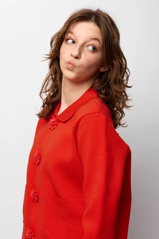 Young woman in red sweater looks sideways with playful expression. Studio portrait on white background. Concept of casual fashion, youth, and personality.
