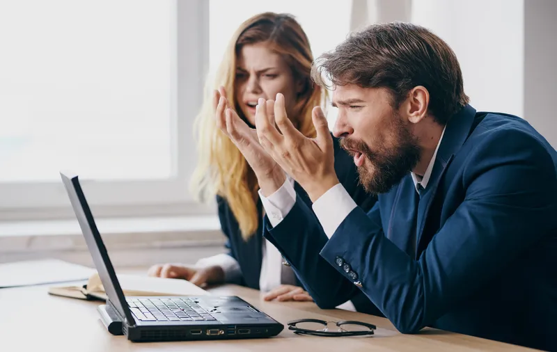 Мужчина и женщина работают за столом с ноутбуком, используя технологии, в офисе, передавая эмоции и общаясь