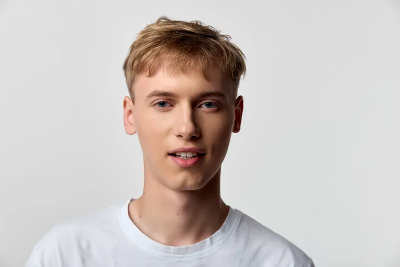 Close up of a young man in a white t shirt with a relaxed expression, clean studio backdrop, soft lighting, and natural pose suitable for lifestyle, fashion, or tech content, minimal styling,