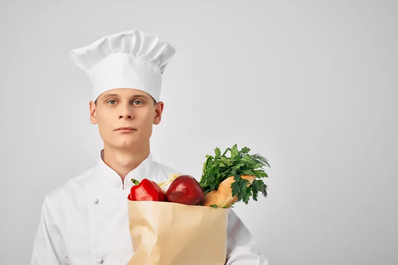 Мужчина в поварской форме с пакетом продуктов работает на кухне ресторана