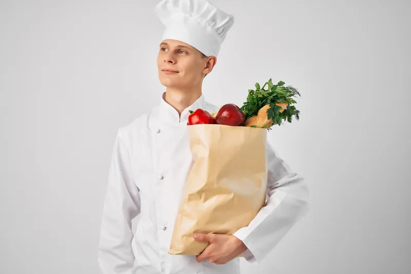 Мужчина в форме шеф-повара с упаковкой продуктов занимается приготовлением пищи в рамках ресторанной работы