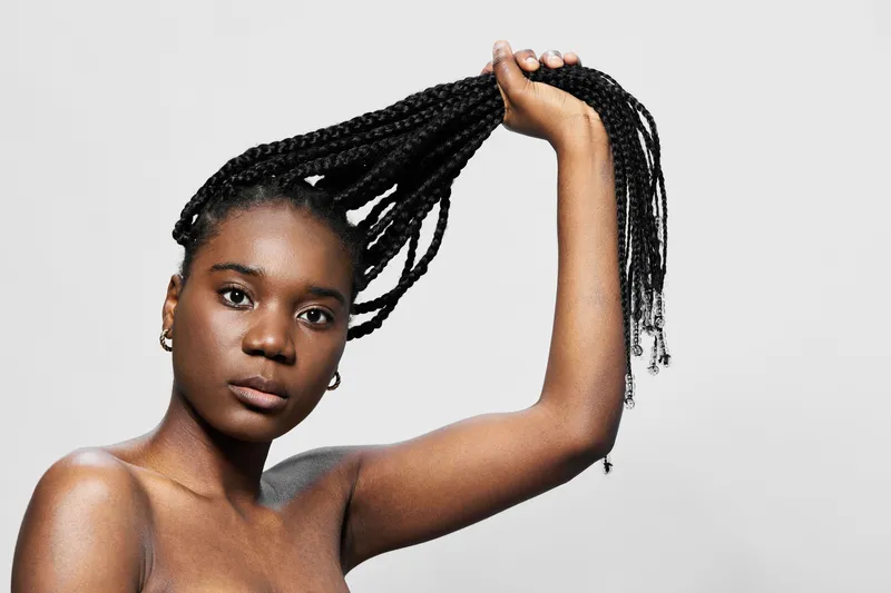 Young African woman with braided hair showcasing confidence and beauty against a neutral background, emphasizing natural beauty and hairstyle trends