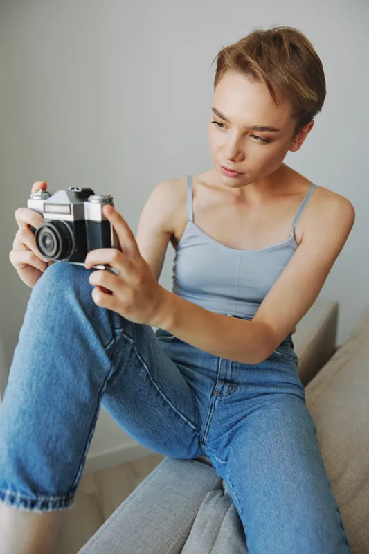 Женщина-фотограф снимает в студии на старую плёночную камеру, сидя на диване дома