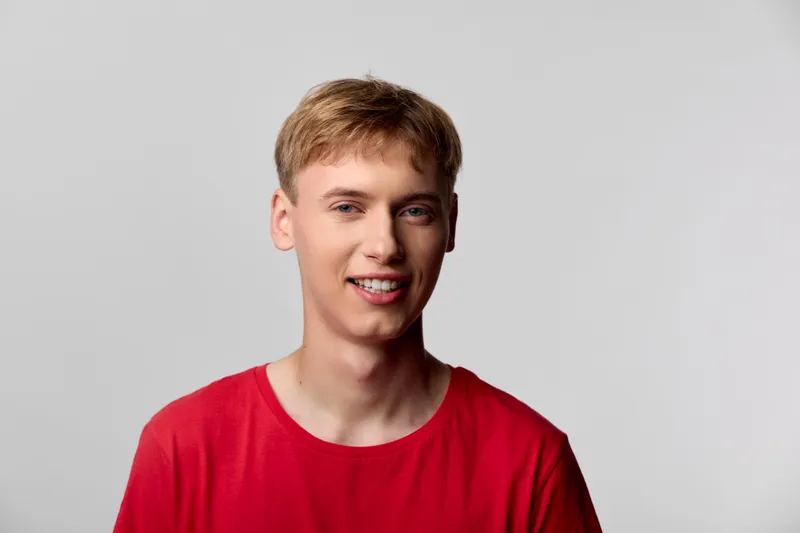 Bright, friendly young man in a red shirt smiles at the camera, creating a vibrant, approachable image for lifestyle, fashion, and social media marketing campaigns.