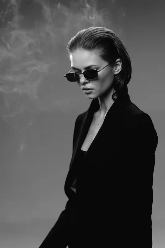 Stylish woman in sunglasses wearing black outfit with smoky background in black and white portrait