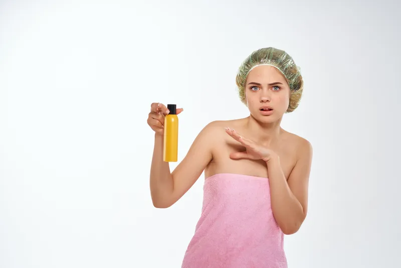 Женщина в розовом полотенце держит желтую баночку с кремом для тела