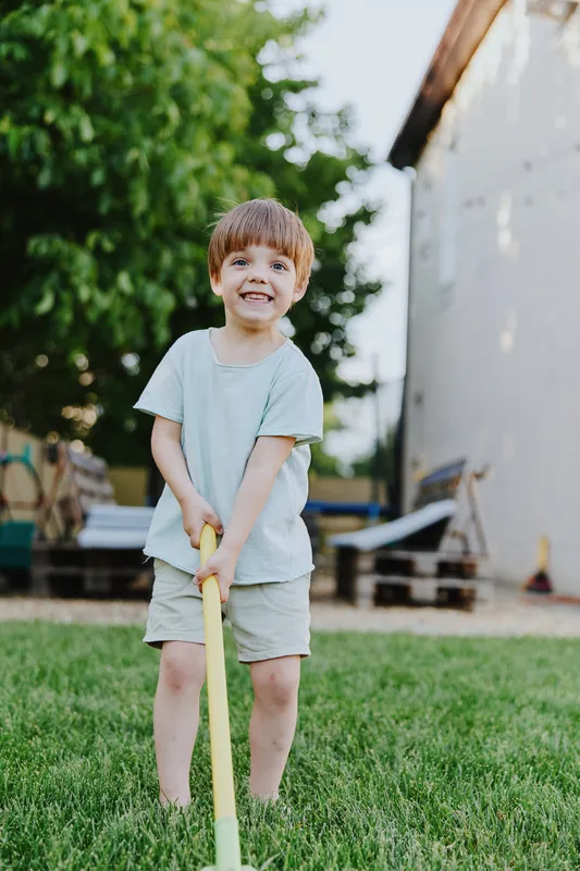 Cheerful boy playing outside, enjoying a sunny day with a playful expression, dressed in a comfortable outfit, surrounded by green grass and trees.
