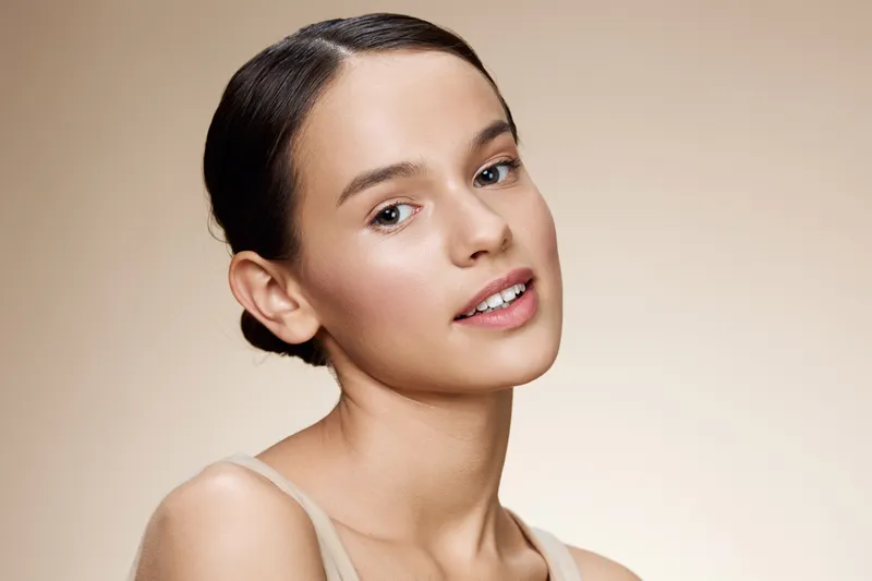Natural beauty portrait of a young woman with a neutral background showcasing healthy skin, soft makeup, and a gentle expression, perfect for beauty and skincare concepts