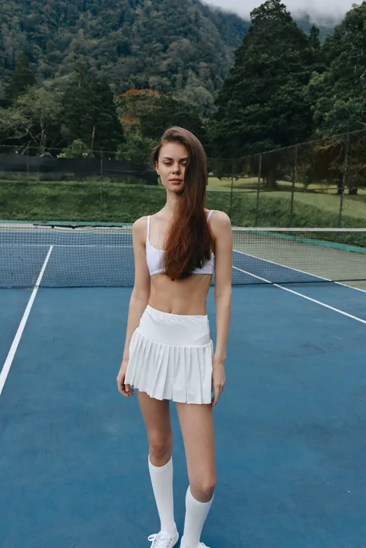 Young athletic woman in sporty outfit poses confidently on tennis court, showcasing vibrant energy and determination, ideal for sports and fitness themes