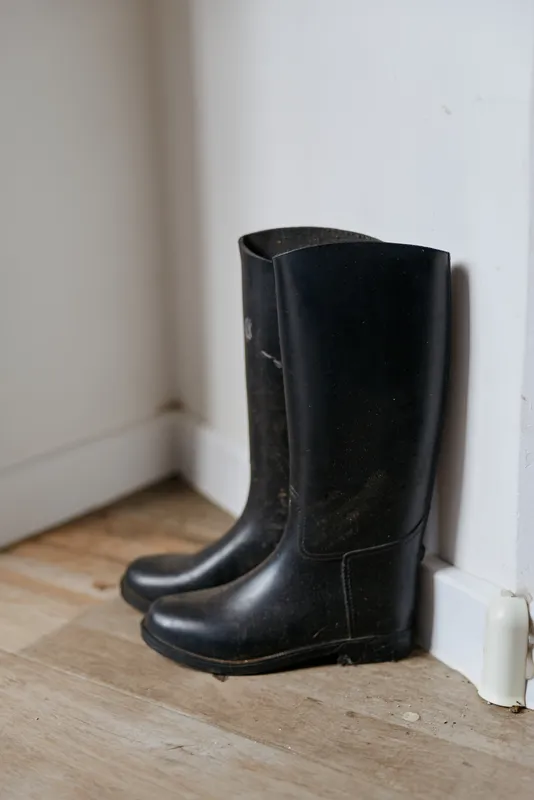 An image of boots in a hallway shows black boots resting by a white wall, embodying home life, calm routine, and the quiet mood of everyday life at home.