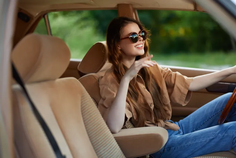 Stylish young woman enjoying a road trip in a vintage car, showcasing a carefree attitude and summer vibes with a warm color palette and vibrant background.