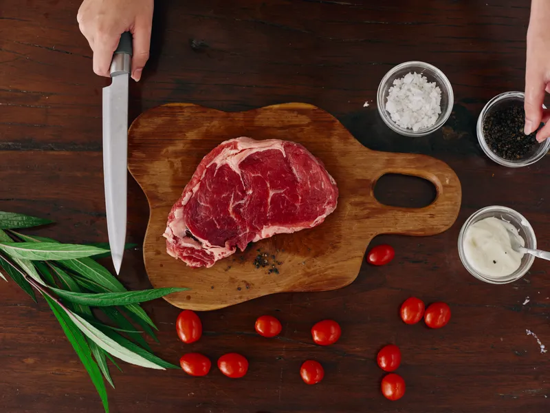Женщина с ножом в руке нарезает свежее мясо стейка для жарки на кухне