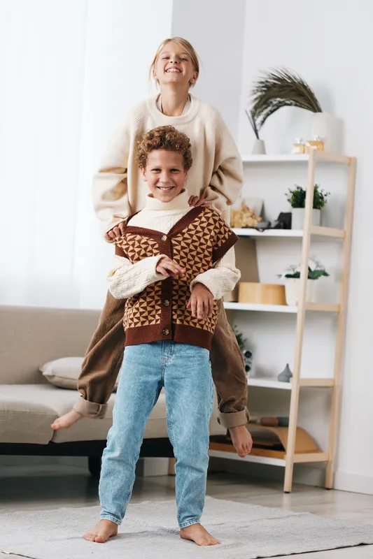An authentic moment of playful school life as two children share laughter and balance during a cozy home scene, radiating warmth, friendship, and everyday activity.