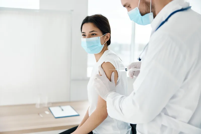 Пациентка в медицинской маске и врач делают инъекцию шприцем для вакцинации
