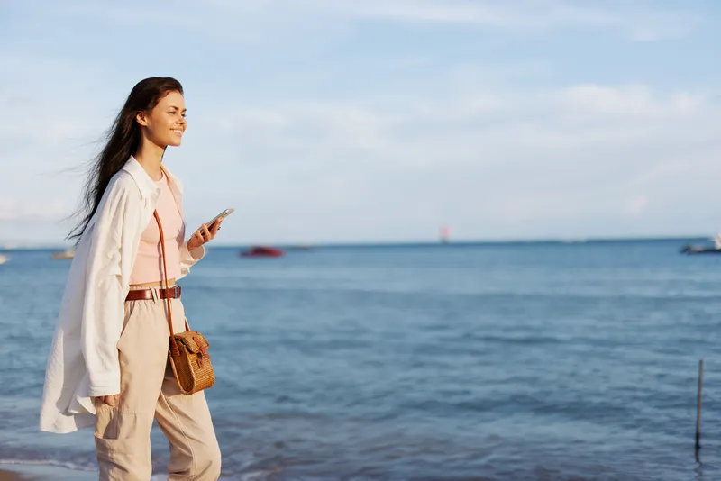 Женщина-фрилансер с телефоном в руке идет в отпуске по пляжу у океана на Бали