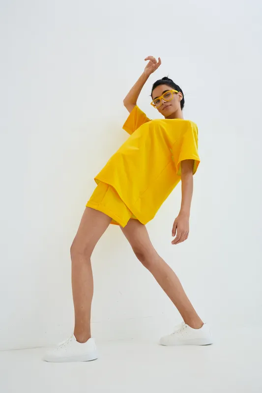 young woman in bright yellow casual outfit and glasses posing dynamically against plain white background with minimalistic modern style and confident vibe