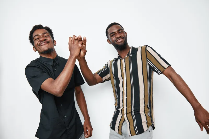 Two young black men with dark skin smiling and shaking hands in casual clothes on white background. Friendship, happiness and connection between african ethnicity males.