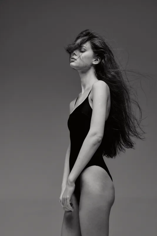 Black and white portrait of a young woman with long hair in a swimsuit against a clear sky.