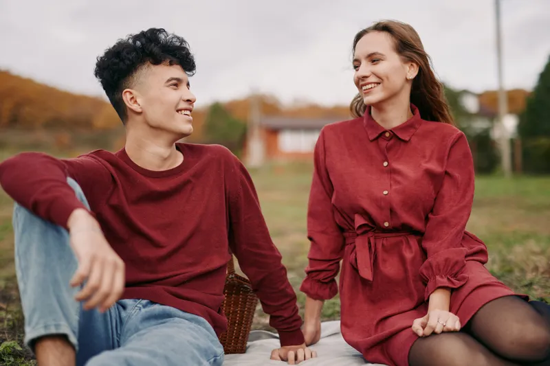Young couple sit on a picnic blanket in an autumn park, sharing a candid smile and natural connection that highlights authenticity and credibility in a relaxed everyday moment.