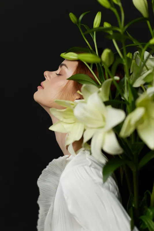Young woman with flowers on a dark background, expressing serenity and beauty, wearing a white blouse Ideal for seasonal and wellness themes