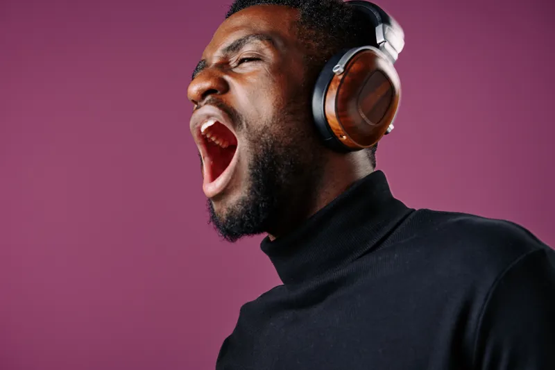 Young Black man passionately singing with headphones on a vibrant purple background, showcasing emotion and music engagement