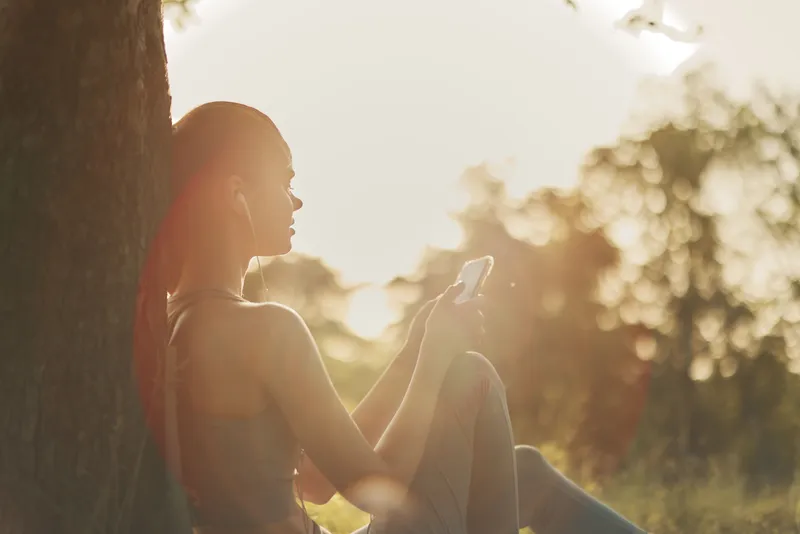 Young woman enjoying music on her smartphone outdoors in the golden hour, reflecting relaxation and connection with nature