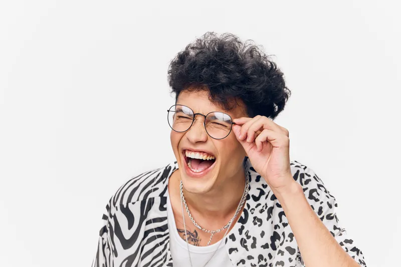 laughing man with curly hair and glasses wearing a zebra print shirt on white background expressing joy and happiness in casual style