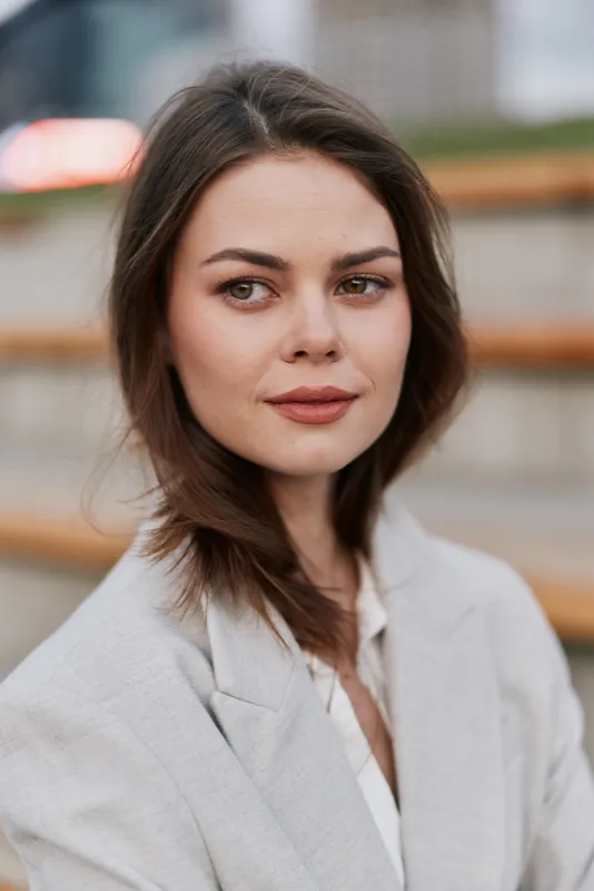 Woman portrait with confident expression in light blazer outdoors, natural brown hair, soft makeup, and muted background perfect for business theme