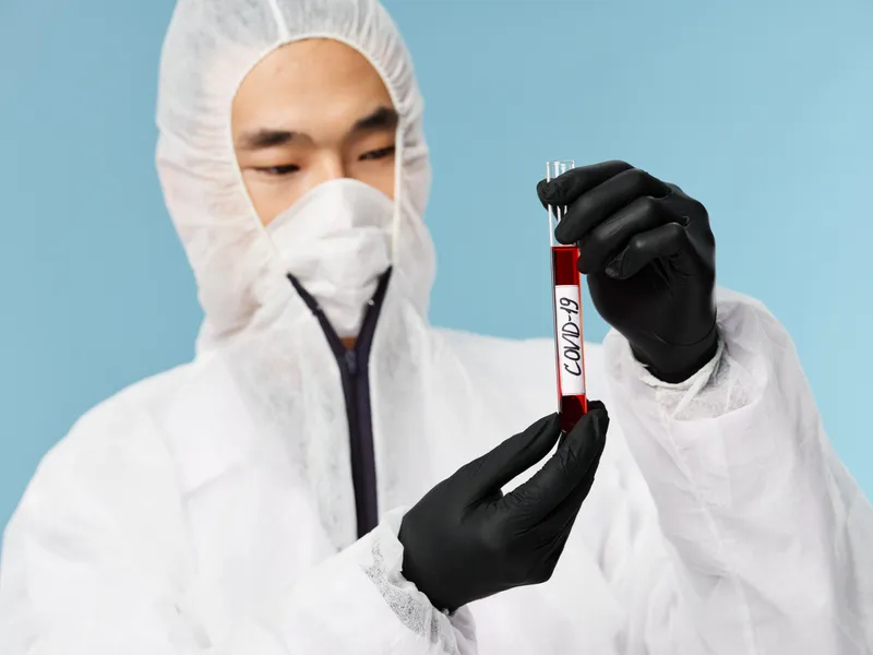 Пациент азиатской внешности, мужчина, сдает анализ крови на COVID-19 на синем фоне