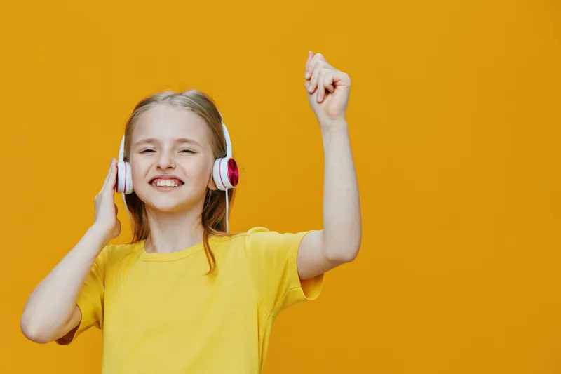 A joyful young girl in a bright yellow shirt and headphones dancing happily against a vibrant yellow background, celebrating music and positivity