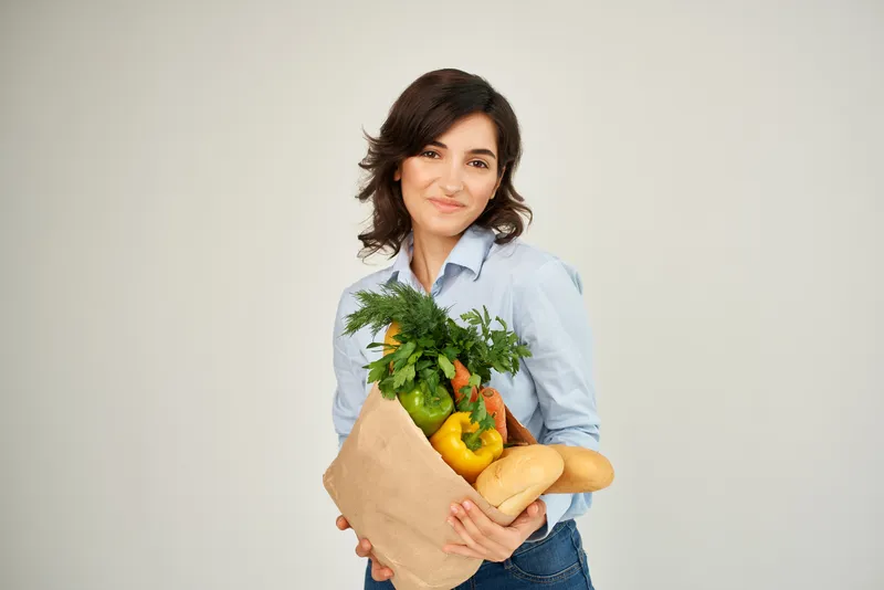 Жизнерадостная женщина с пакетом продуктов в супермаркете, образ жизни