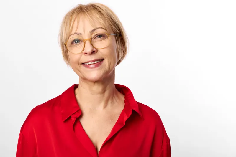 Senior woman portrait in studio with smiling expression wearing red blouse and glasses on white background calm confident look closeup headshot of mature female