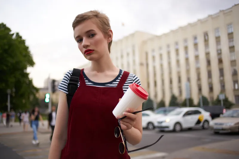 Женщина на открытом воздухе с чашкой напитка, в очках, разговаривает по телефону