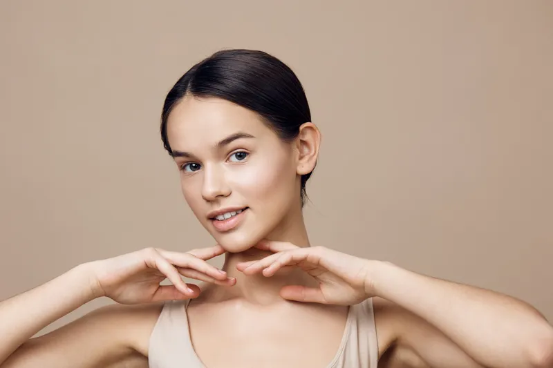 Young woman with natural makeup and smooth skin, expressing confidence and beauty on a neutral beige background Facial care, health, and wellness concept