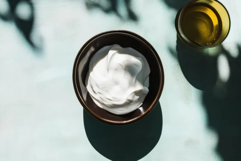 Аппетитная миска с creamy йогуртом в сопровождении стакана оливкового масла на фоне листовой зелени