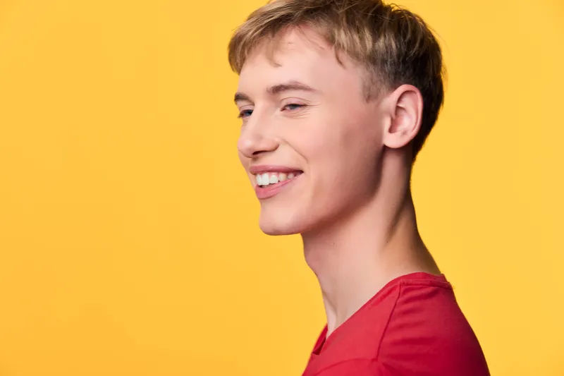 Smiling man in a red shirt against a bold yellow backdrop, conveying warmth, approachability and positive mood suitable for lifestyle, marketing, or corporate communications imagery.