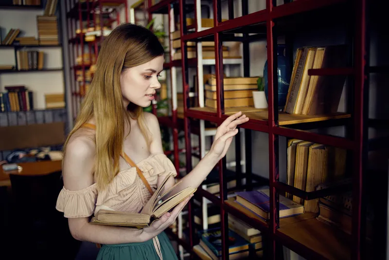 Симпатичная женщина ищет книгу в библиотеке и читает во время отпуска