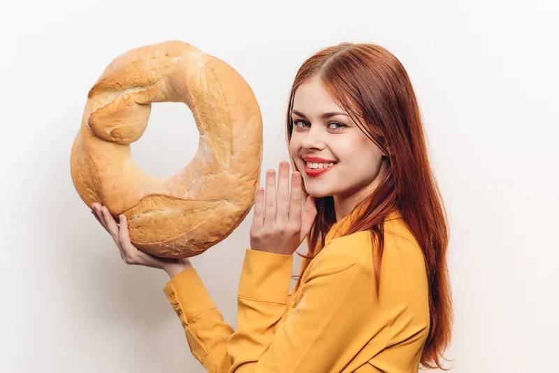 Мучное изделие, круглая буханка хлеба и эмоциональная женщина в желтой рубашке