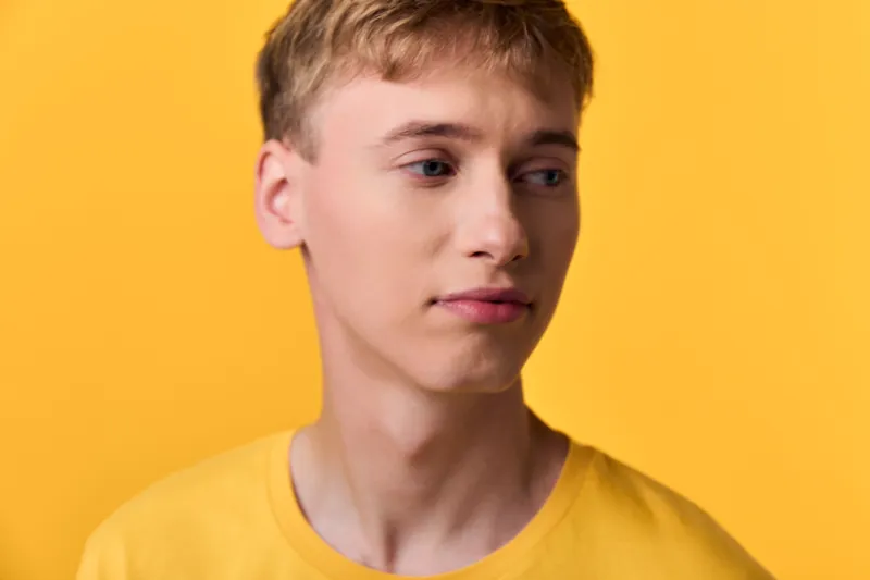Young man with thoughtful gaze against a vivid yellow backdrop, wearing a matching yellow tee. Studio lighting highlights smooth skin, clean lines, and a minimal fashion mood for modern lifestyle