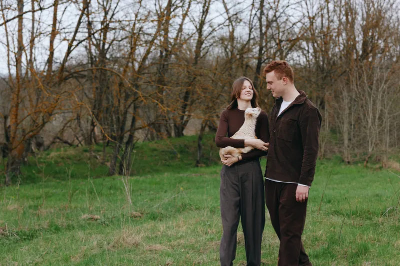 A couple outdoors with a goat kid in a grassy field, smiling at each other. A warm, candid lifestyle moment in a natural setting, perfect for family, animals, and nature themed storytelling.
