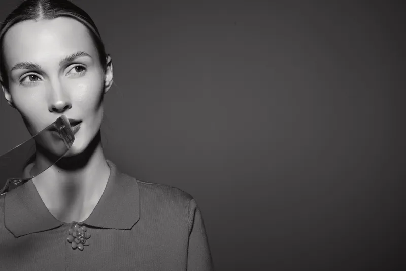 Portrait of a fair skinned Caucasian woman with slicked back hair holding transparent sheet near face in black and white studio. Concept for beauty and fashion.
