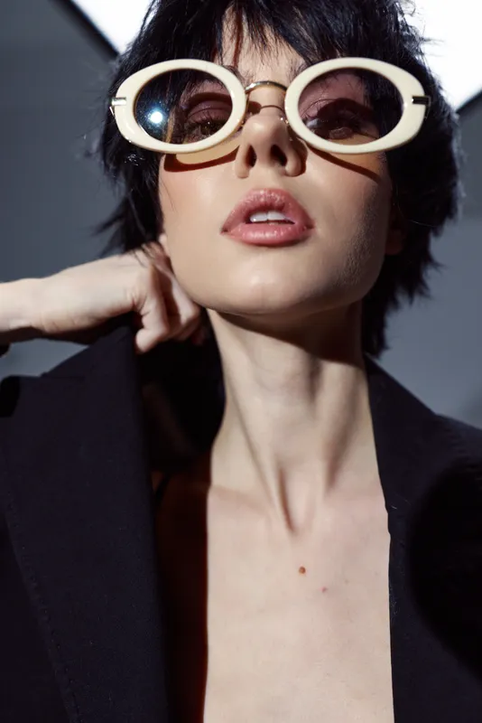 Stylish woman wearing oversized white sunglasses and dark clothing with a confident expression and modern fashion vibe