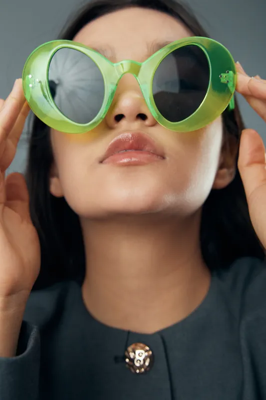 Woman with green oversized sunglasses adjusting eyewear on face closeup. Fashion, style and accessory with modern outfit in portrait for beauty and trend concept.