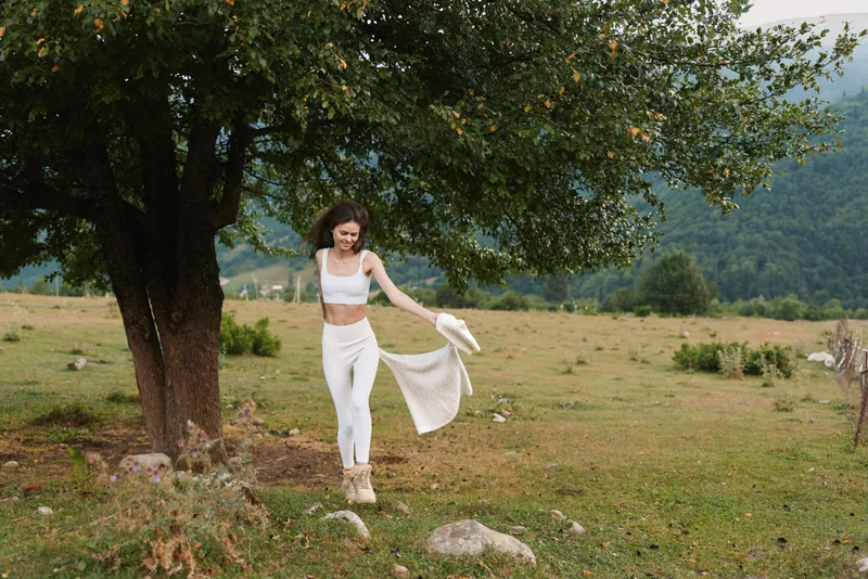 Woman outdoors, joyful moment, lifestyle in a sunlit field beside a tree, she dances with carefree energy, bright light, and natural colors